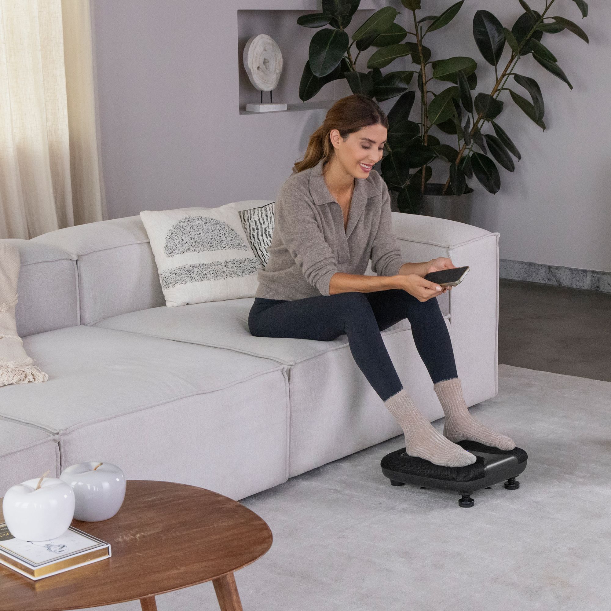 Donna seduta sul divano che utilizza un massaggiatore per piedi nero. Piedi sul dispositivo.