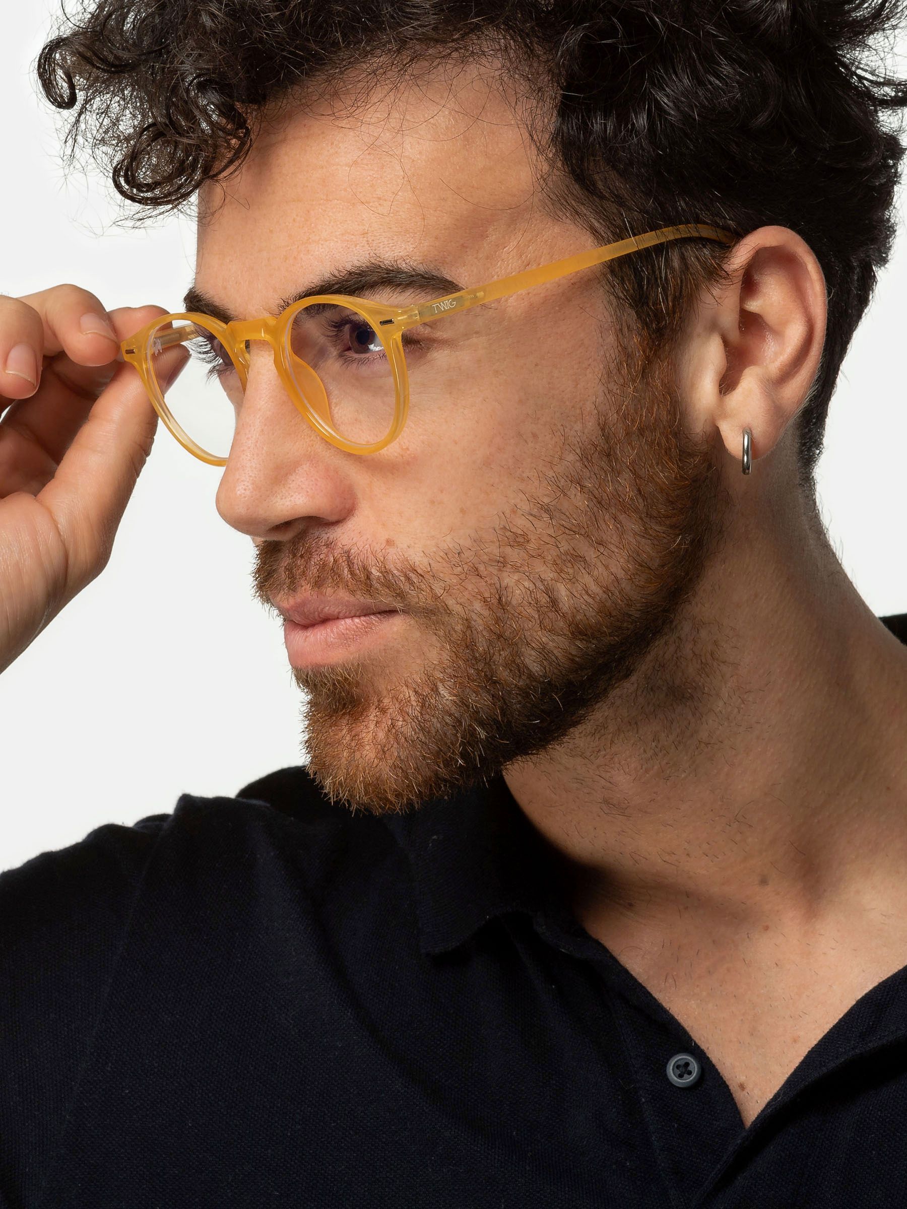 Uomo con occhiali gialli. Lenti rotonde, montatura gialla. Solleva gli occhiali. Camicia scura.