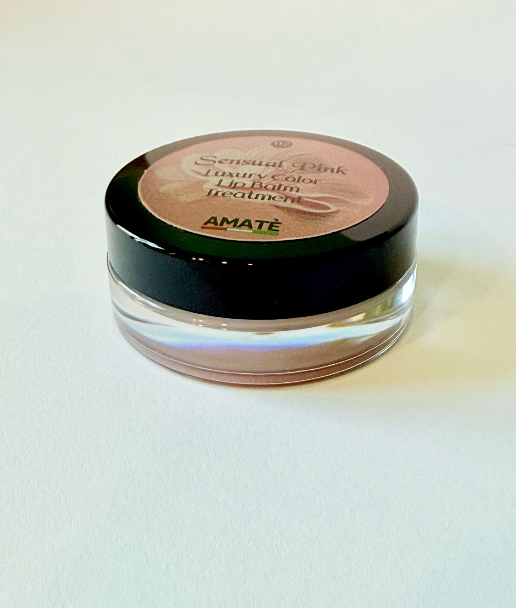 Vasetto rotondo con coperchio nero. Sul coperchio, si legge "Sensual Pink Luxury Color Lip Balm Treatment" e "AMATÈ".