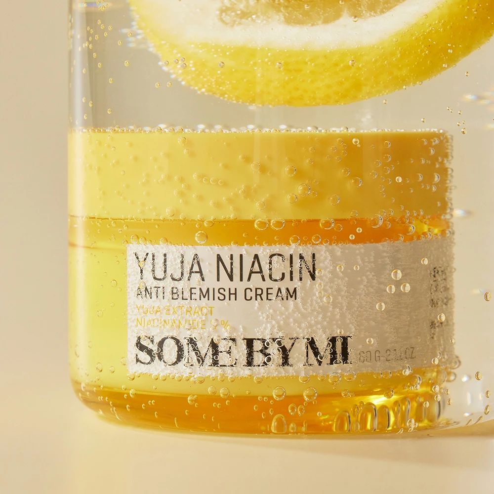 Vasetto giallo SOME BY MI Yuja Niacin Anti Blemish Cream in acqua. Fetta di limone sopra. Bolle.
