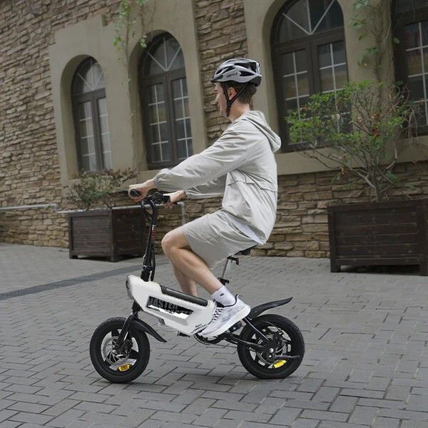 Persona in sella a e-bike pieghevole bianca e nera. Indossa il casco. Sfondo: strada, edifici.