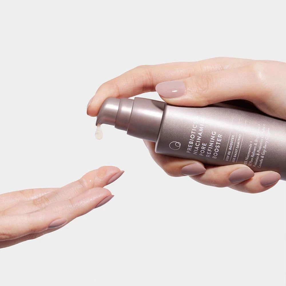 Mani che tengono una bottiglia. Liquido che gocciola sul palmo. Scritta: PREBIOTICS NIACINAMIDE PORE REFINING BOOSTER.