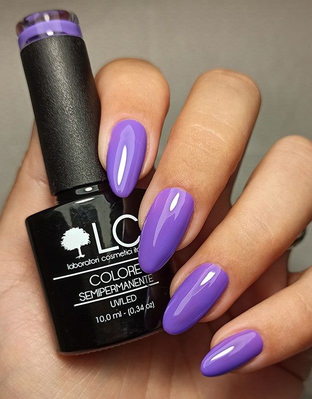 Mano con unghie viola smaltate. Flacone di smalto con scritta: LCI, Colore Semipermanente, UVLED.