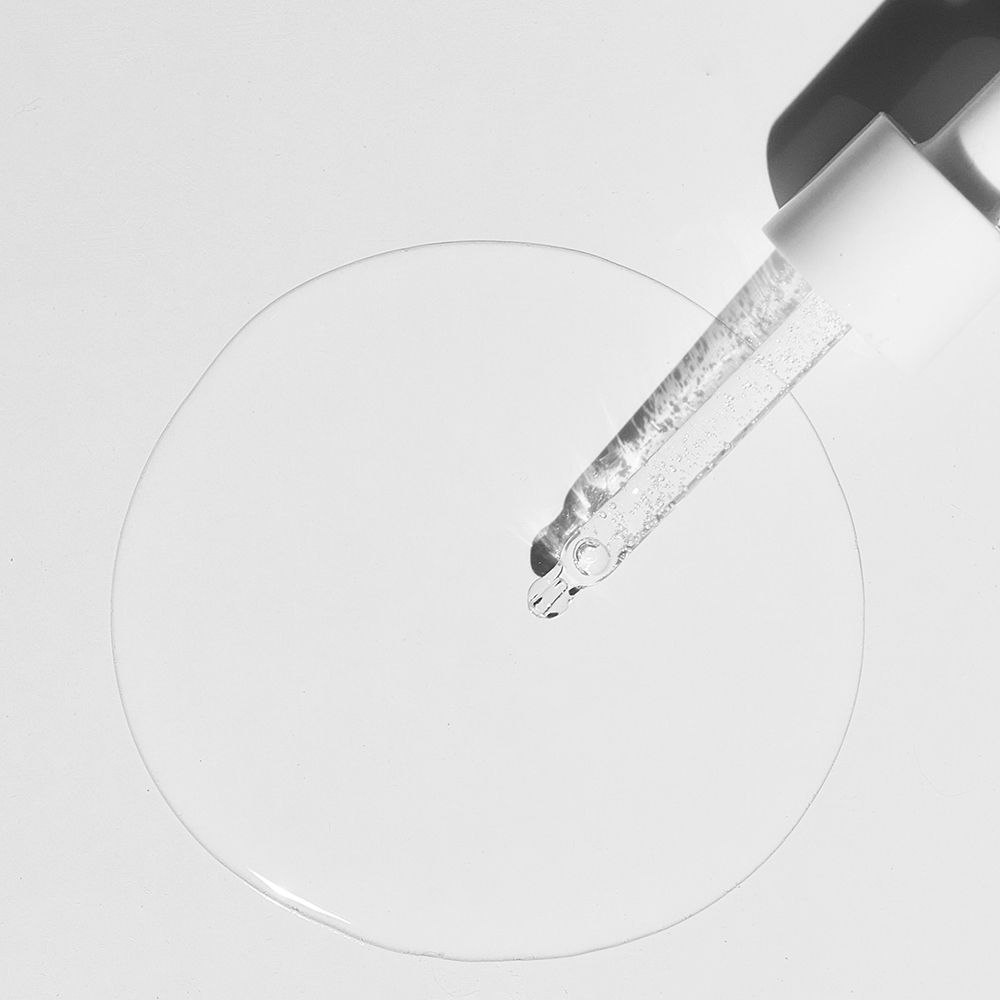 Pipetta con liquido. Il liquido gocciola su una superficie circolare. Sfondo bianco.