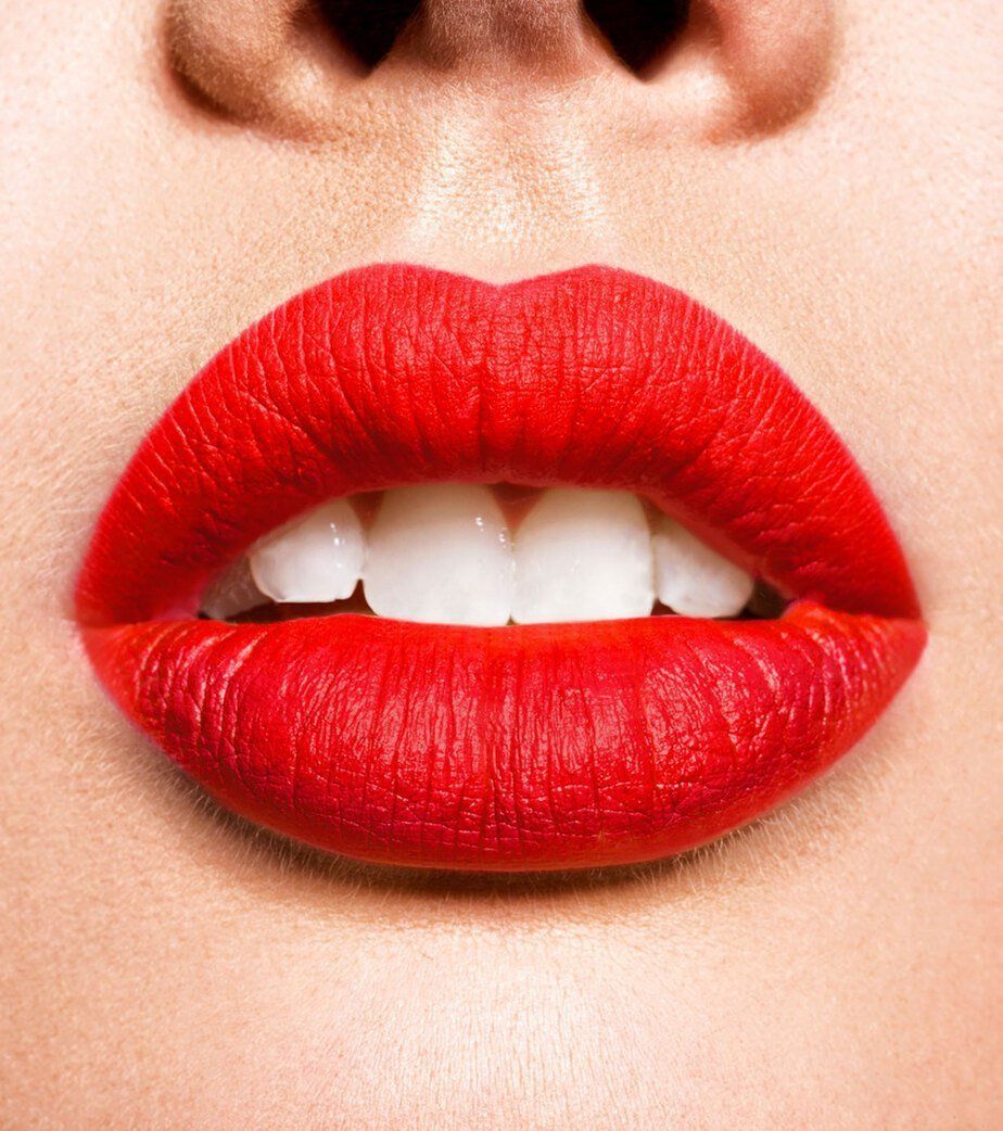 Primo piano di labbra carnose con rossetto rosso e denti bianchi.