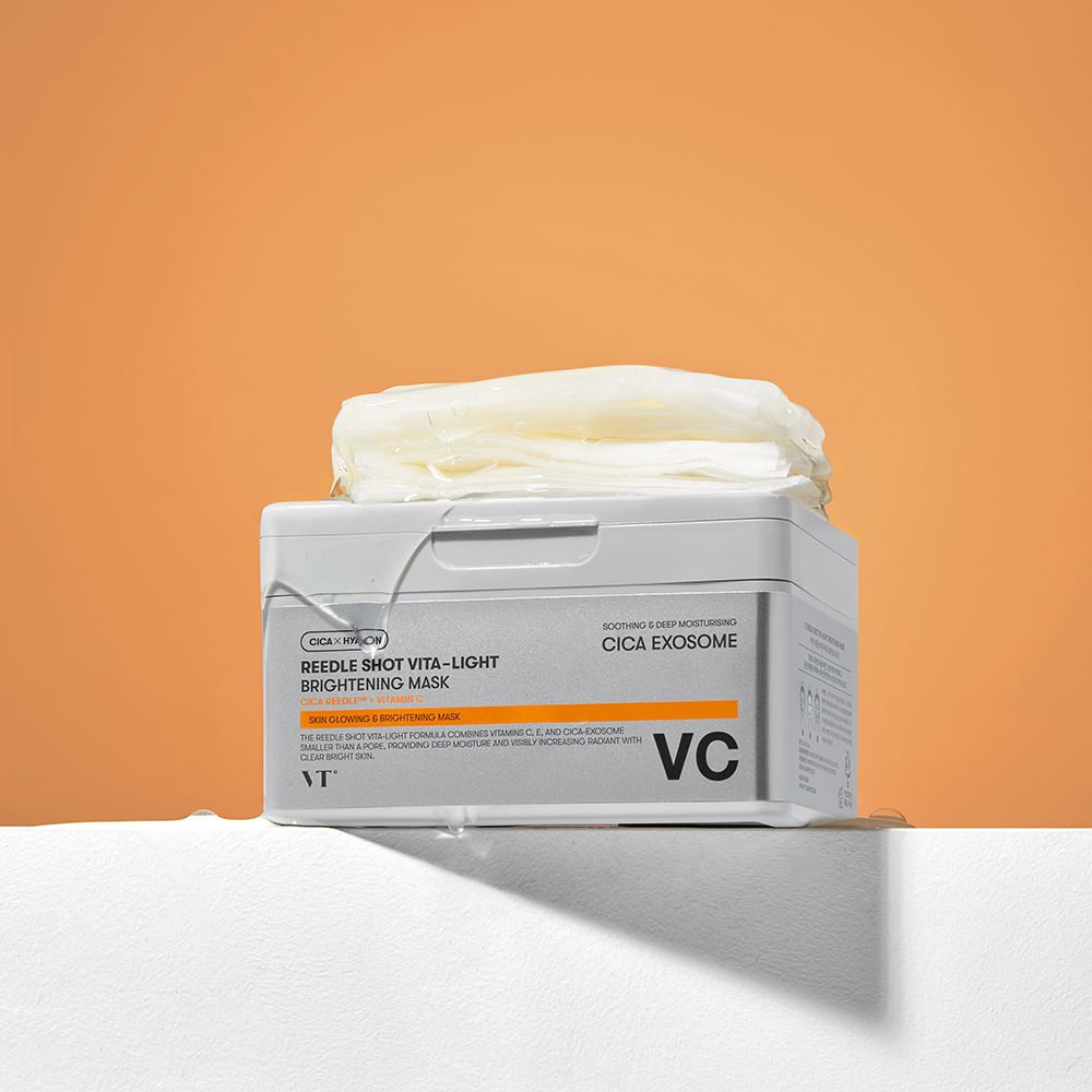 Scatola grigia con maschere su piedistallo bianco, sfondo arancione. Scritta: Reedle Shot Vita-Light Brightening Mask. Marchio: VT.