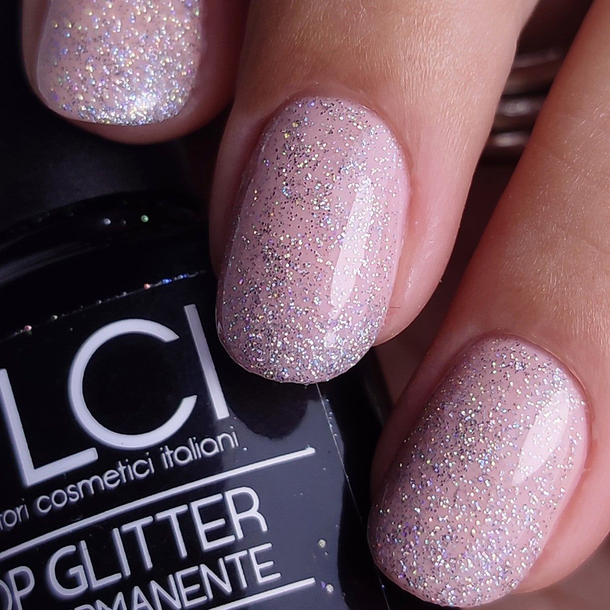 Smalto rosa glitterato sulle unghie. Flacone parzialmente visibile. Scritta: LCI Cosmetics, Top Glitter.