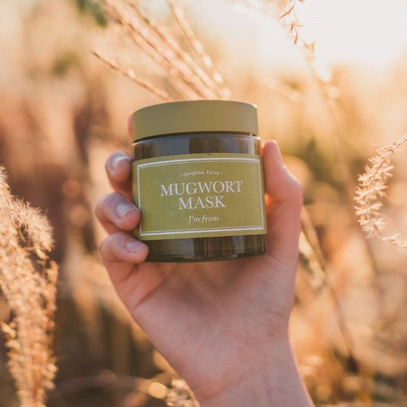 Mano che tiene un vasetto di Mugwort Mask. Testo: Mugwort Mask, I'm from.