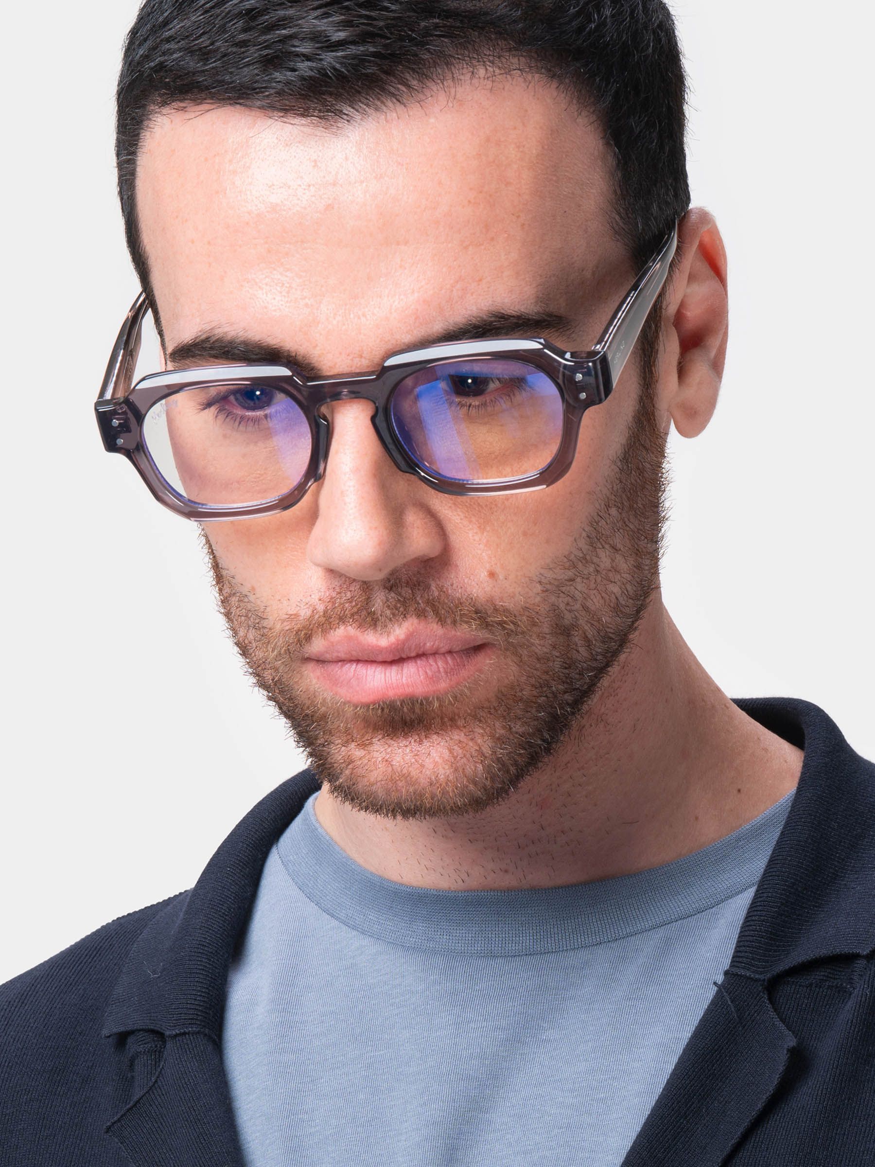 Uomo con occhiali grigi a montatura rettangolare. Primo piano del viso. Camicia blu. Lenti con tonalità blu.