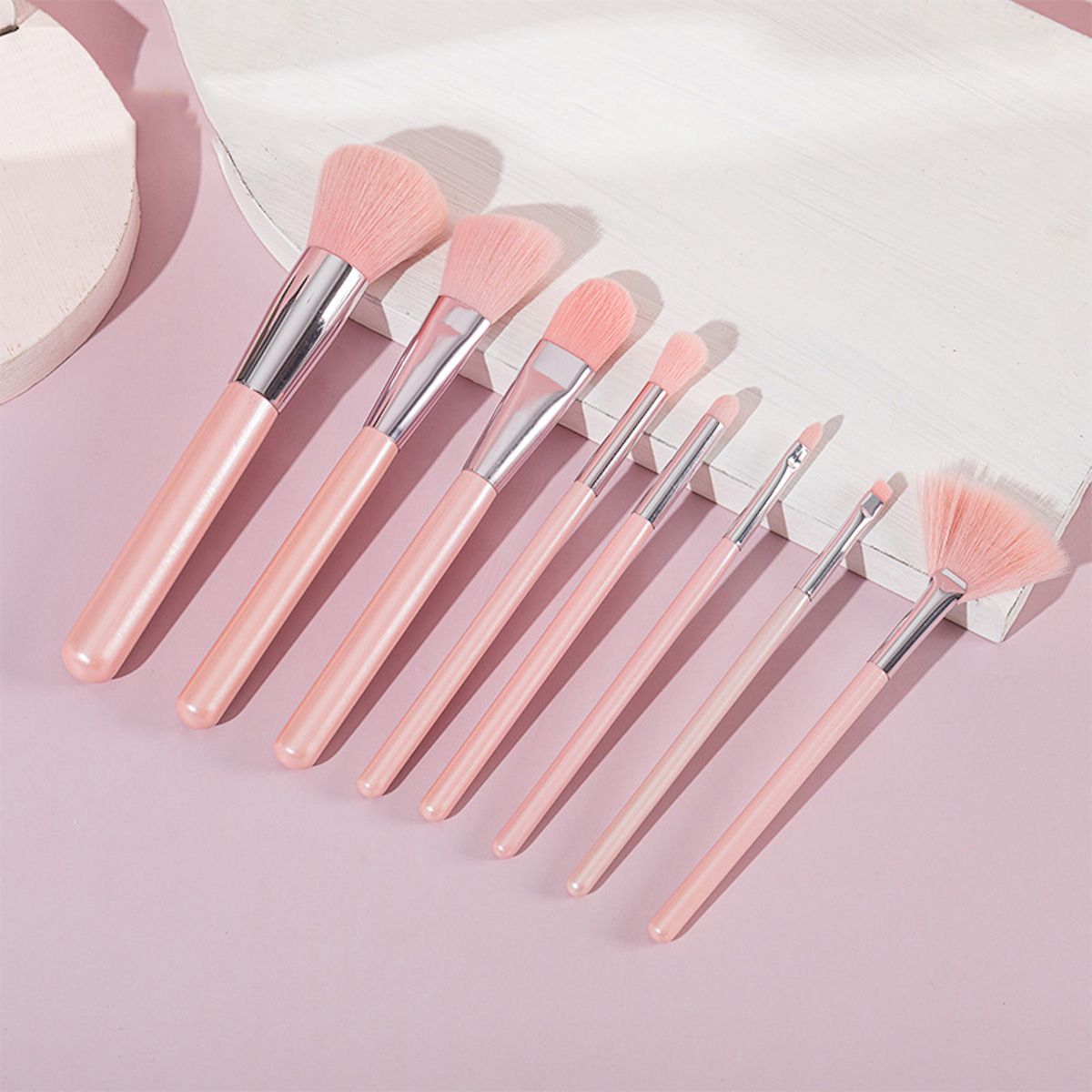Un set di sette pennelli per il trucco rosa con accenti argentati, su una superficie rosa.