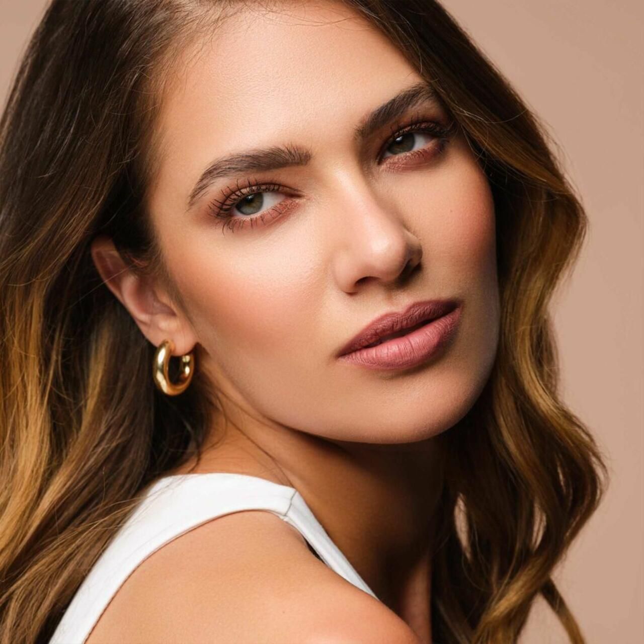 Ritratto di donna con rossetto. Orecchini a cerchio dorati. Tono della pelle. Capelli castano chiaro.