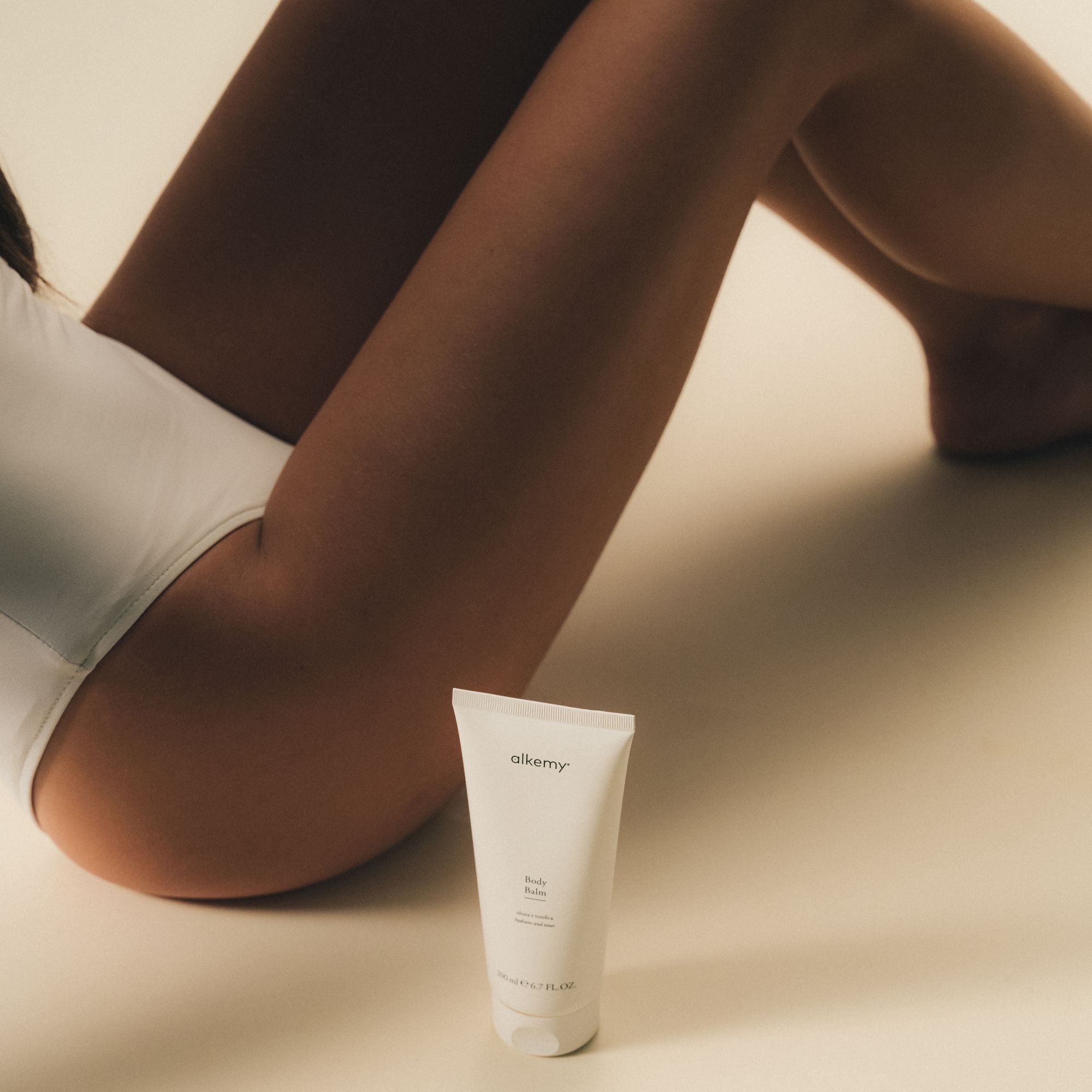 Un tubetto bianco di balsamo corpo posato a terra accanto alle gambe di una persona.