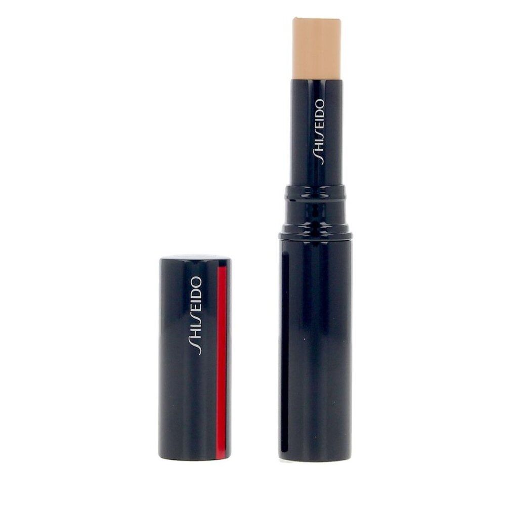 Stick correttore blu scuro con striscia rossa. Tappo accanto. Nome del prodotto e marchio: SHISEIDO. Stick color crema.
