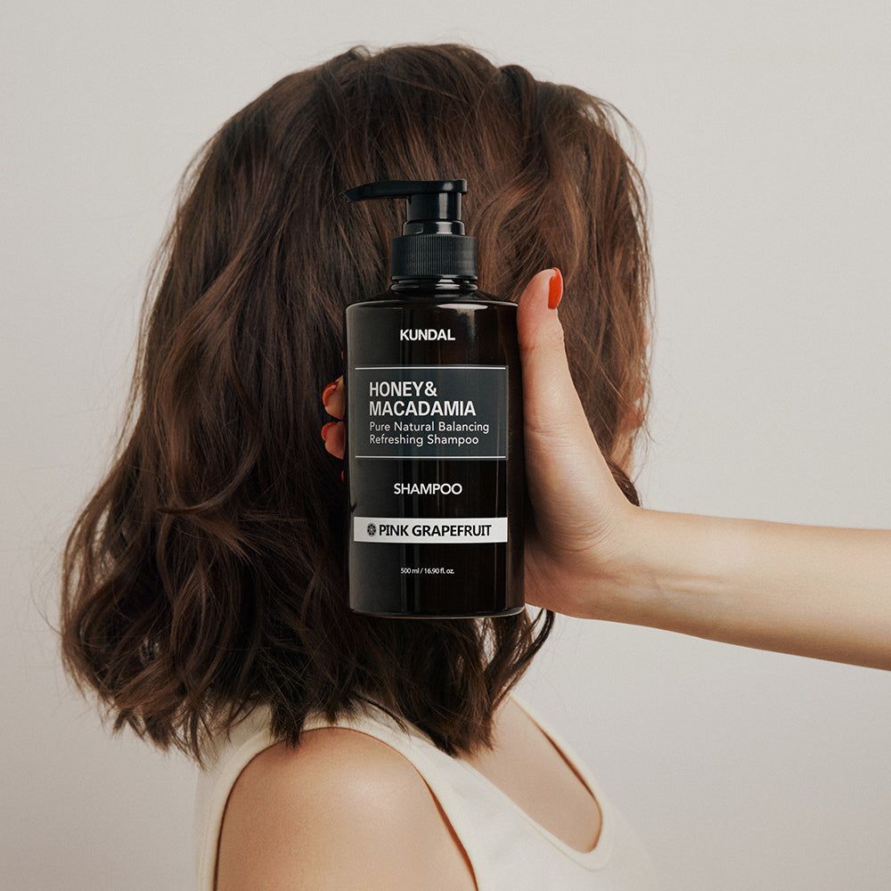 Una mano tiene un flacone di shampoo marrone davanti ai capelli di una persona.