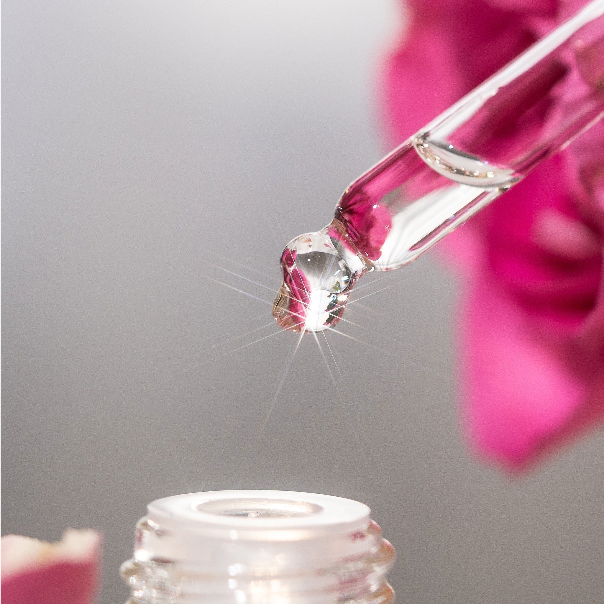 Primo piano di una pipetta con una goccia. Il liquido gocciola in un flacone. Sfondo: fiore rosa.