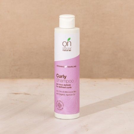 Flacone shampoo. Tappo bianco, etichetta rosa con testo: Curly Shampoo, Officina Naturae. Con olio di albicocca bio.