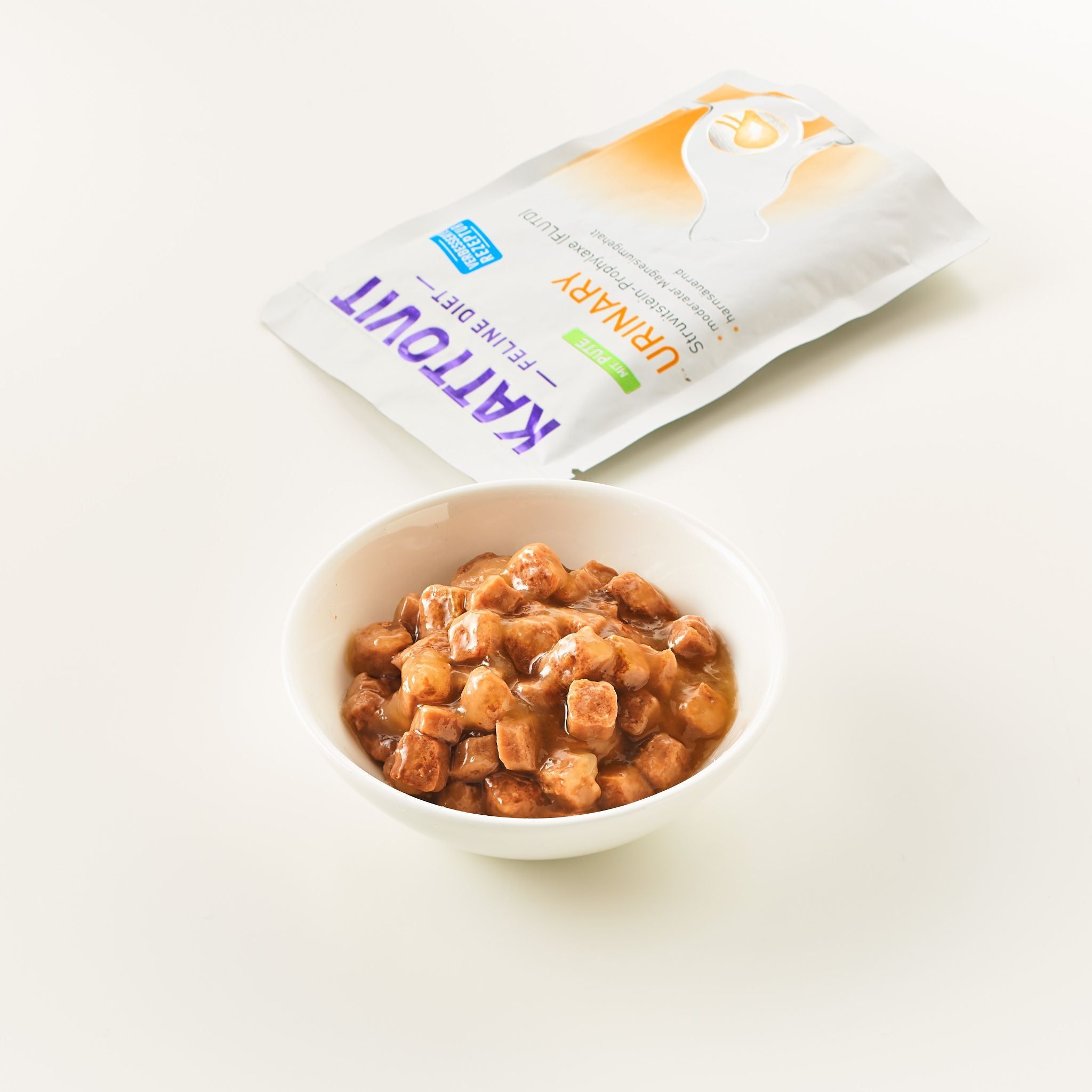 Ciotola con cubetti di cibo accanto a una bustina KATTOVIT Urinary. Scritta: KATTOVIT Feline Diet Urinary. Sfondo bianco.