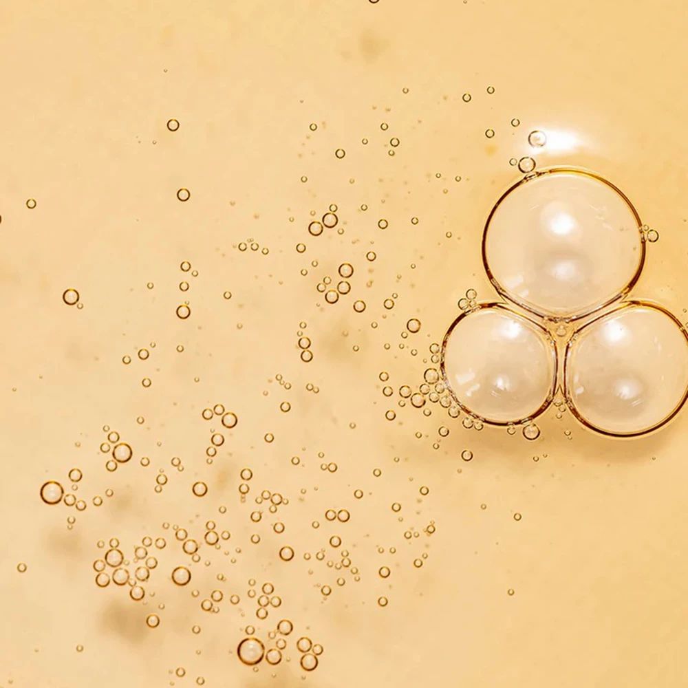 Primo piano di bolle in un liquido giallastro. Alcune bolle grandi, altre piccole.