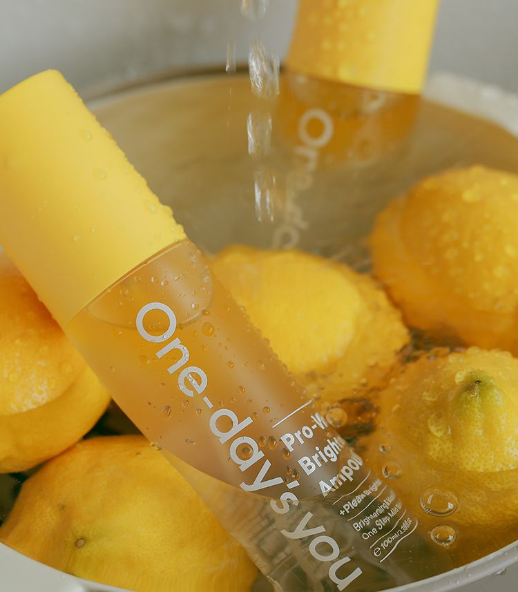 Flacone spray giallo con scritta "One-day's you", circondato da limoni in acqua.
