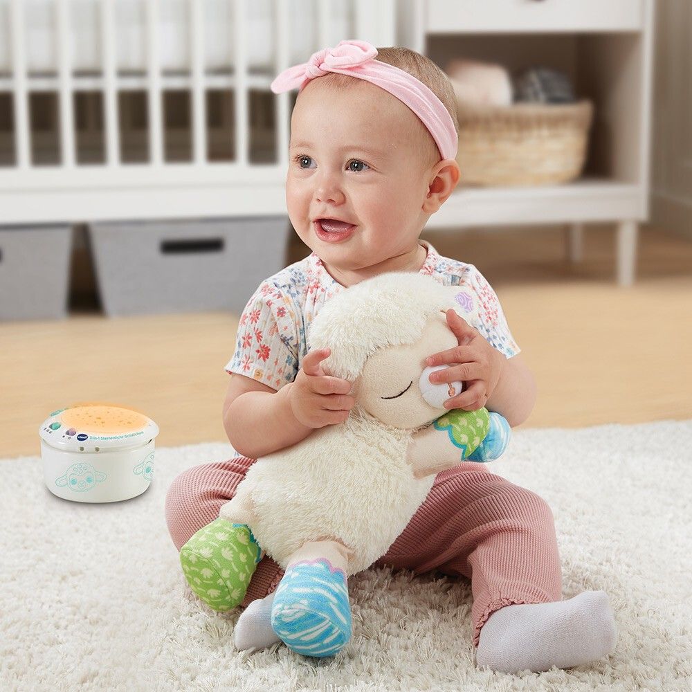 Bambino piccolo tiene in mano una luce notturna a forma di pecora bianca. Un proiettore rotondo accanto.