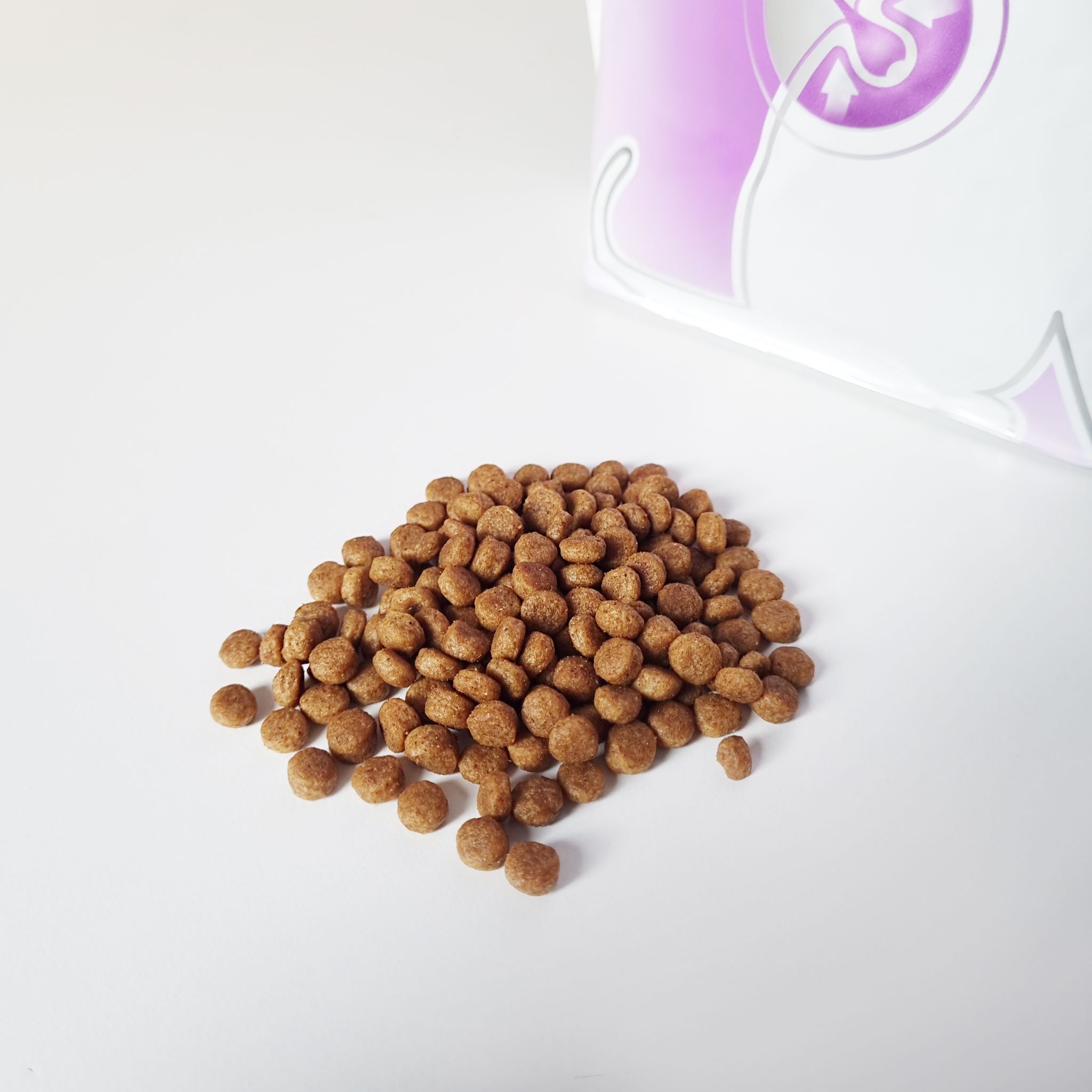 Mucchio di crocchette secche rotonde e marroni. Parzialmente nell'immagine: confezione KATTOVIT Sensitive Trockenfutter.