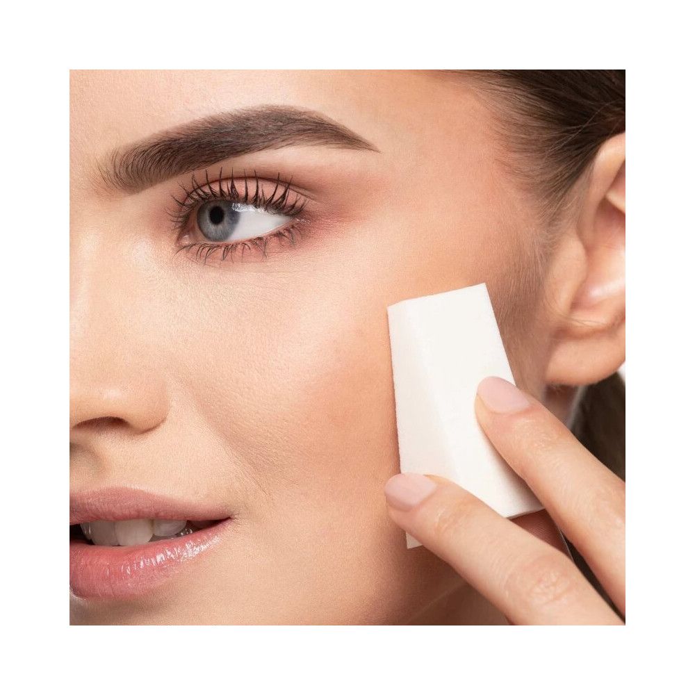 Una donna usa una spugnetta per trucco triangolare sulla guancia.