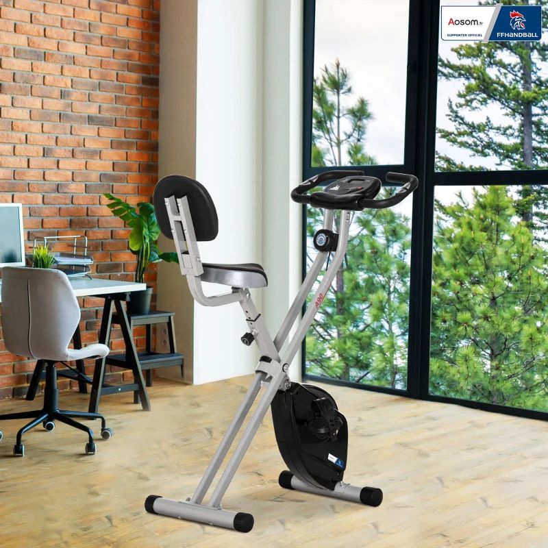 Cyclette in una stanza. Visibili finestre, scrivania, sedia e muro di mattoni.