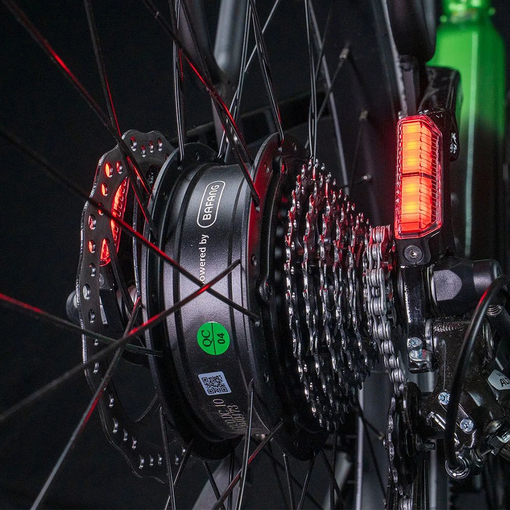 Primo piano della ruota posteriore. Catadiottri rossi, freno a disco e catena. Scritta: Powered by Bafang.