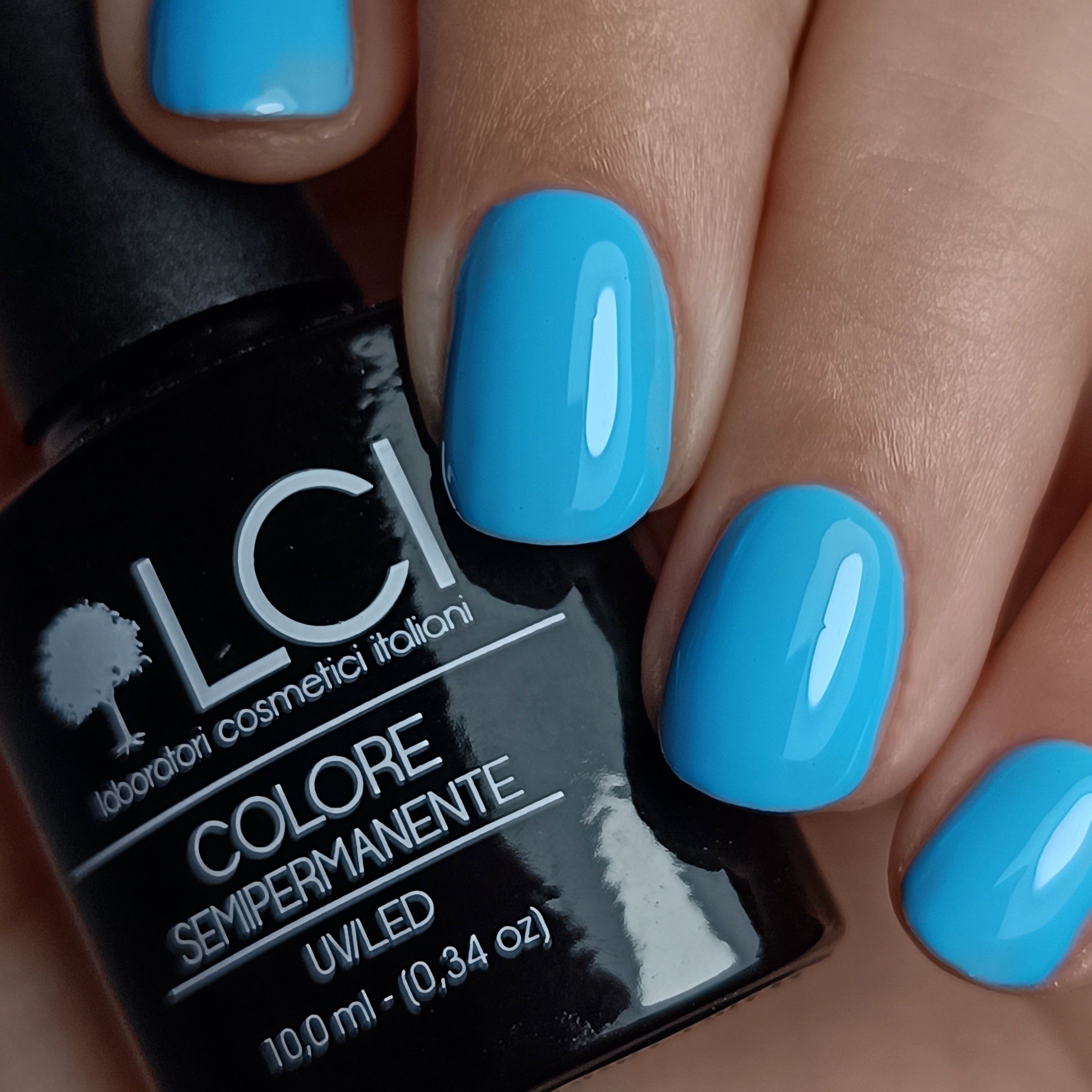 Mano con unghie smaltate e flacone di smalto. Scritta: LCI, Colore Semipermanente, UV/LED. Unghie azzurre.