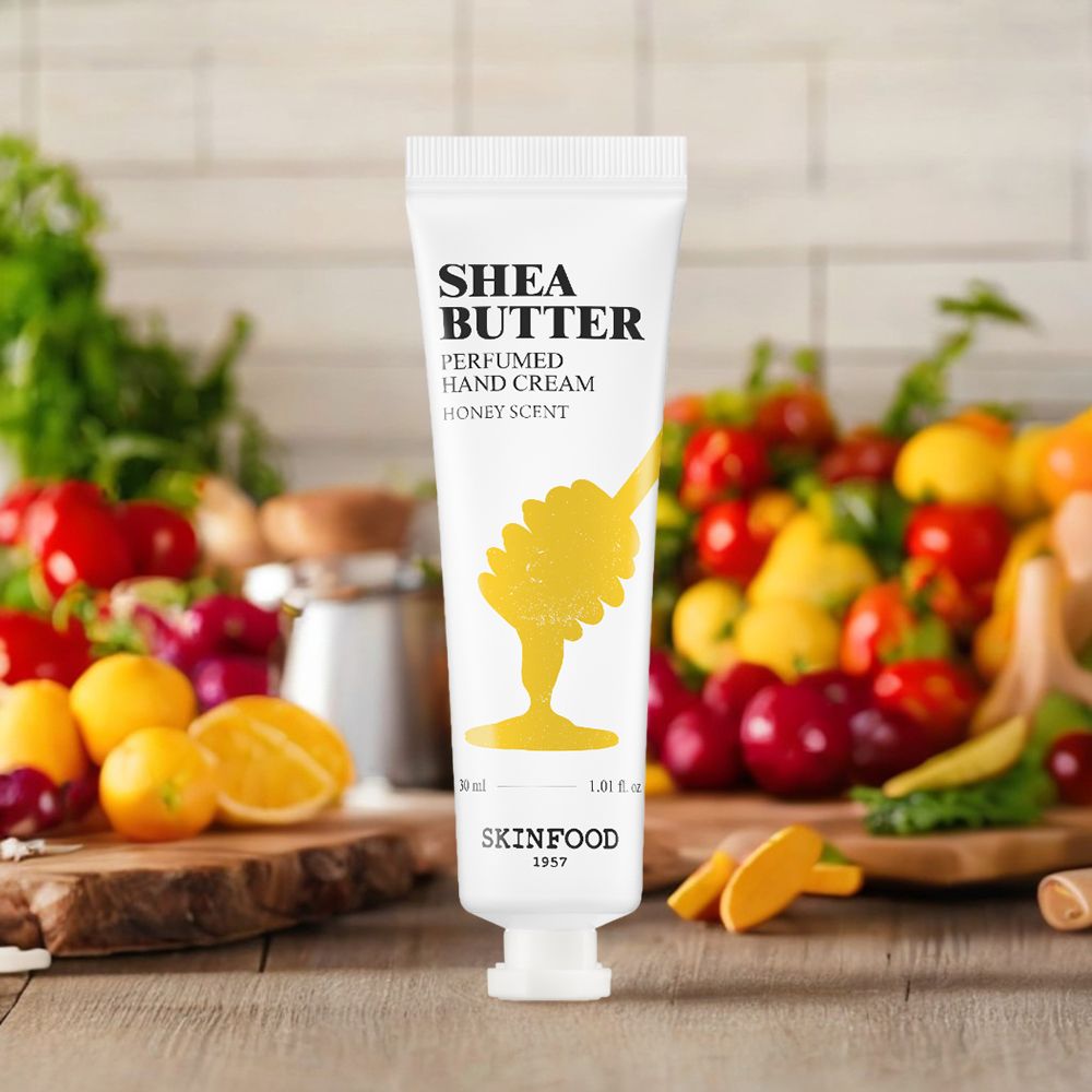 Tubo di crema mani SKINFOOD Shea Butter su sfondo con frutta e verdura. Scritta: Shea Butter, Honey Scent.