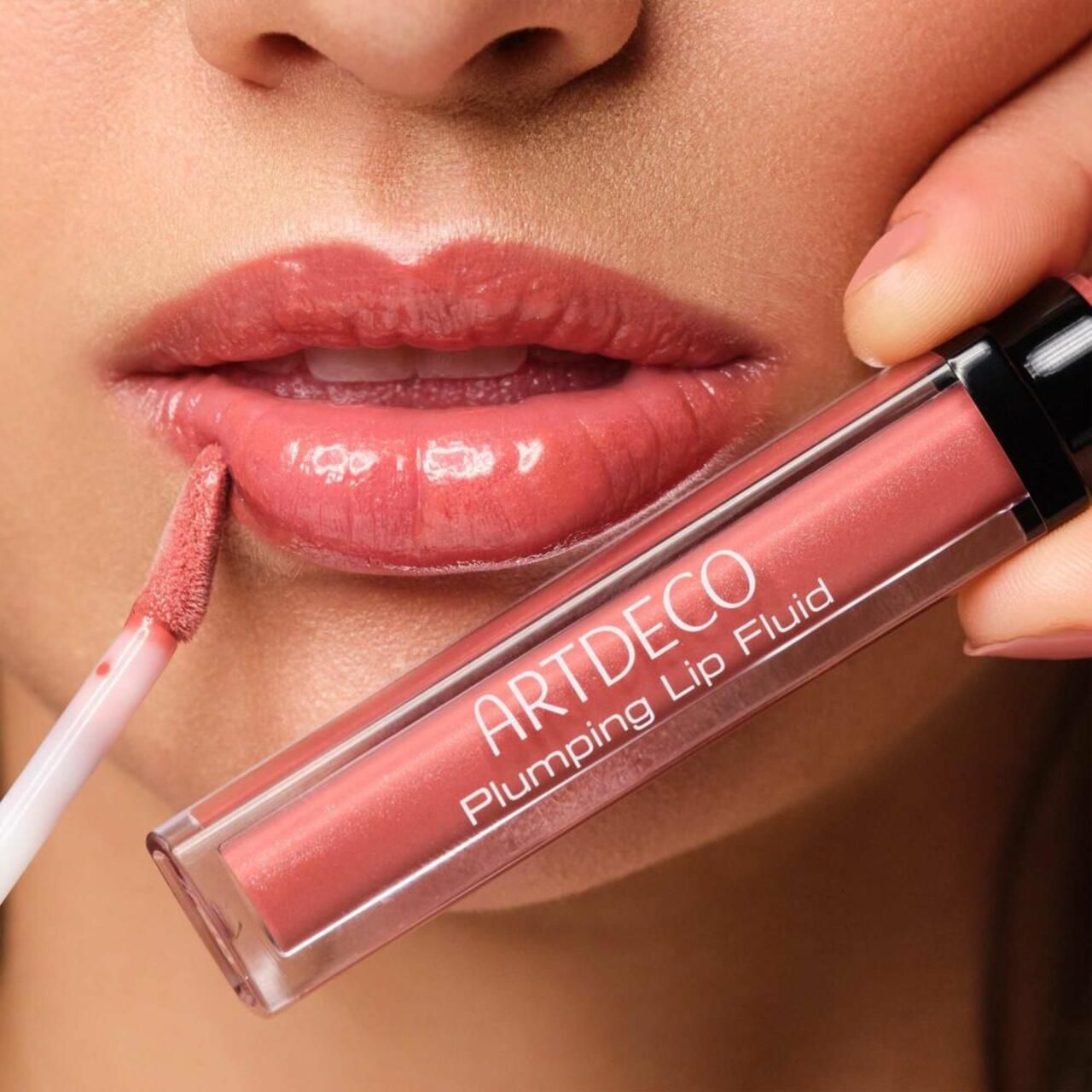 Persona applica Artdeco Plumping Lip Fluid. Prodotto e applicatore visibili. Labbra lucide, rosate.