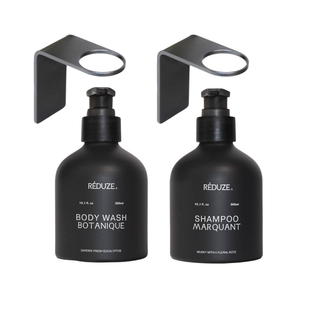 Due flaconi neri con supporti a parete. Scritta: RÉDUZE, Body Wash Botanique, Shampoo Marquant.