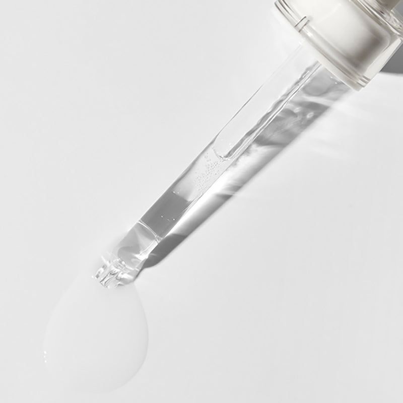 Contagocce trasparente con liquido. Il liquido gocciola su una superficie bianca.