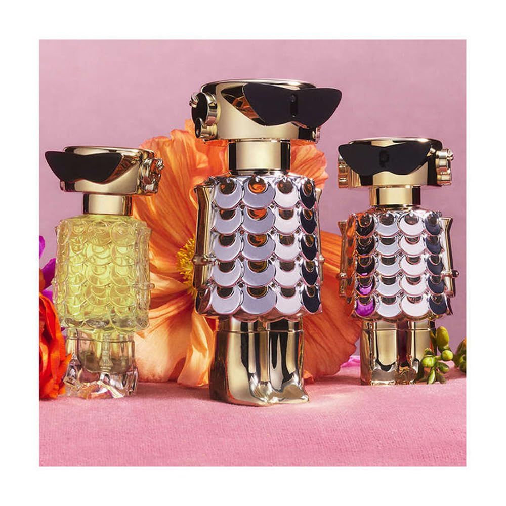 Tre flaconi di profumo a forma di robot. Oro, scaglie argentate, occhiali neri. Fiori sullo sfondo.