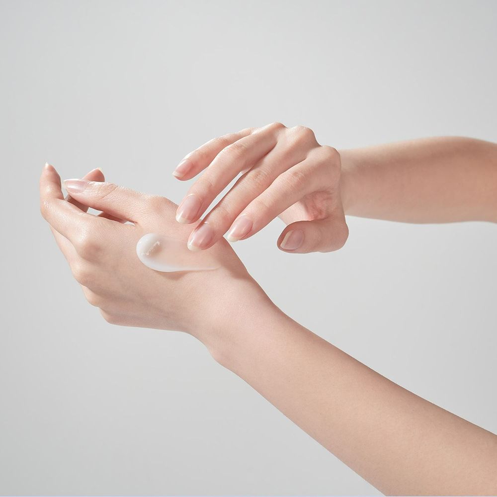 Mani che applicano la crema. Crema bianca sulla mano. Sfondo chiaro.