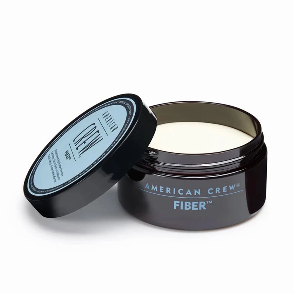 Barattolo blu scuro aperto con "AMERICAN CREW FIBER". Crema per capelli color crema visibile.