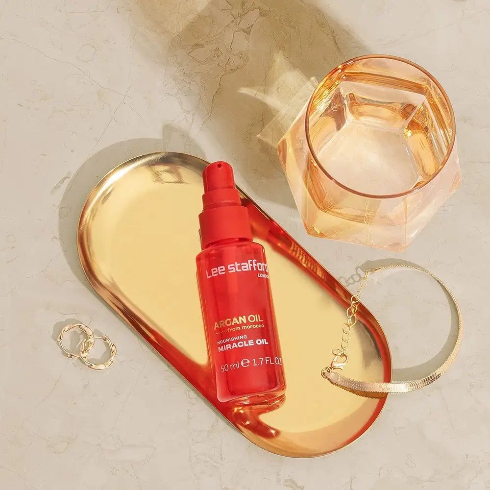 Flacone Olio di Argan Lee Stafford su vassoio dorato con gioielli.