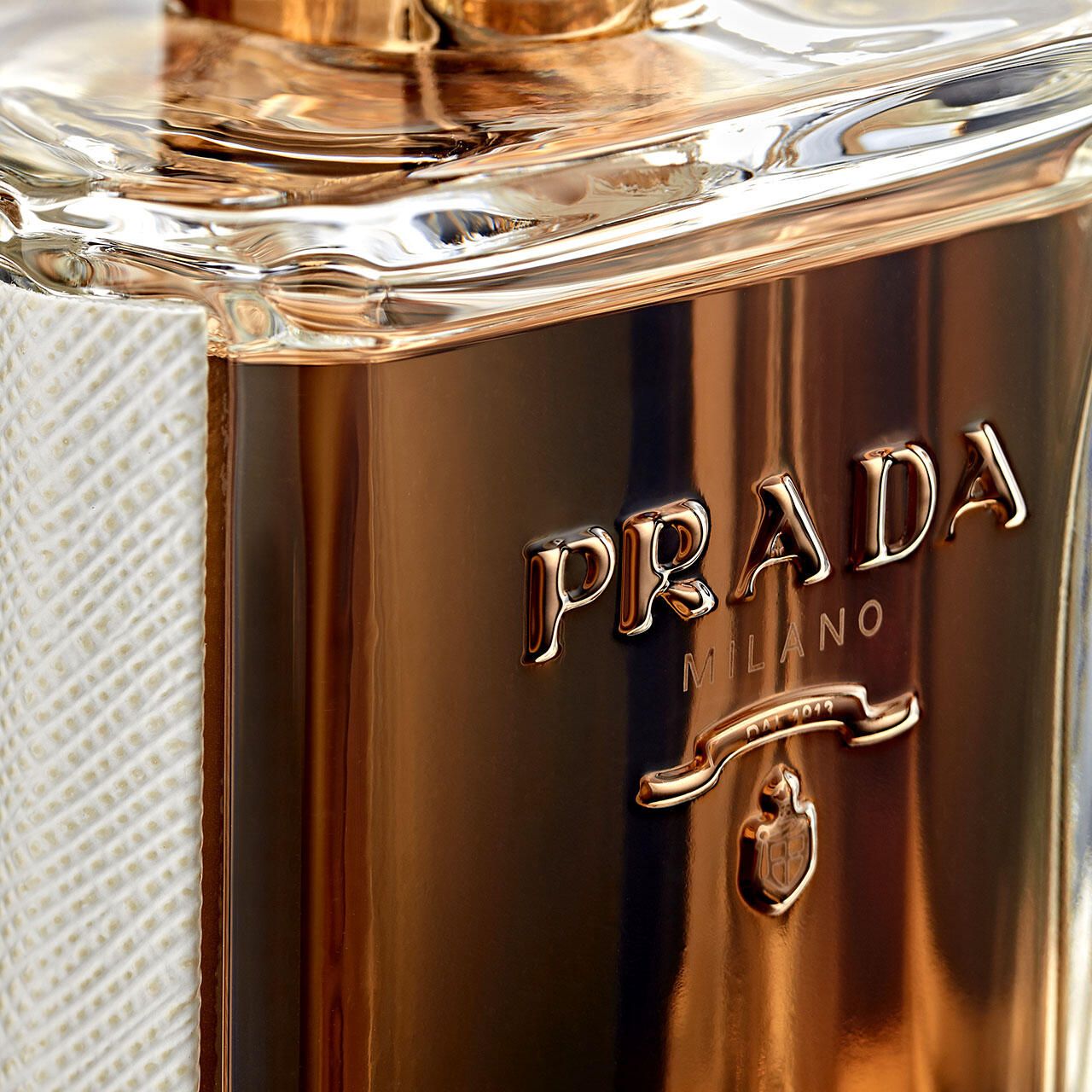 Primo piano del flacone di profumo Prada. Scritta dorata Prada Milano. Liquido dorato all'interno.