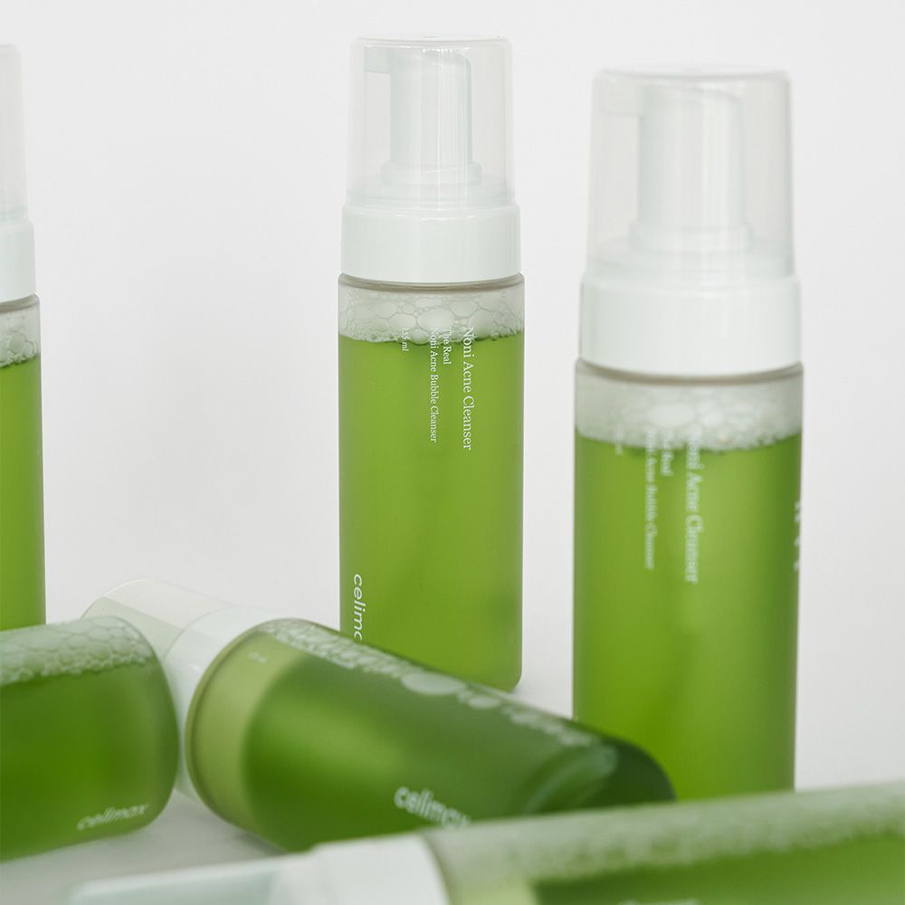 Molteplici flaconi di detergente schiumogeno anti-acne Celimax Noni, alcuni sdraiati, con contenuto verde ed erogatori a pompa.