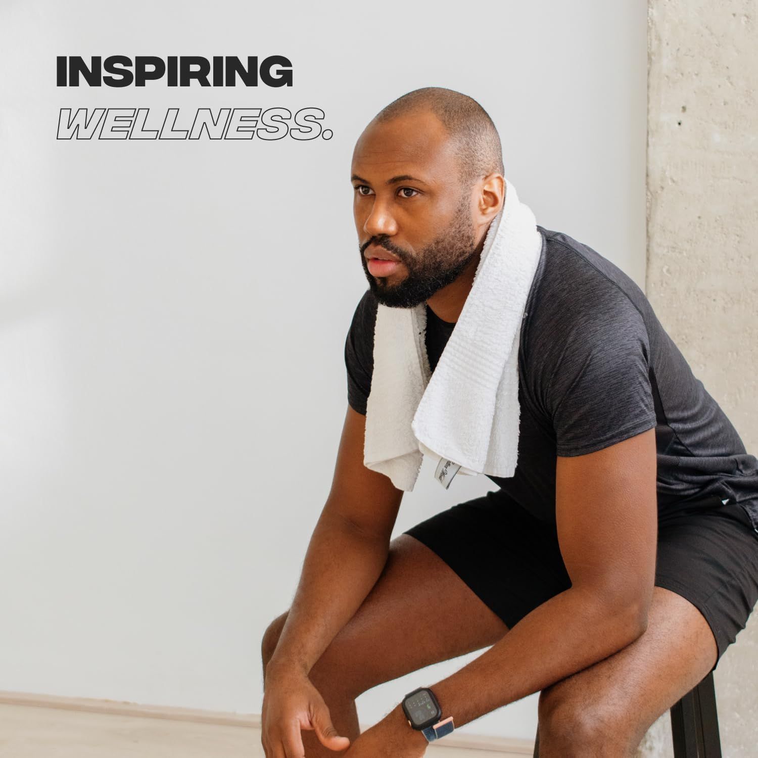 Uomo seduto su uno sgabello, asciugamano al collo. Inspiring Wellness.