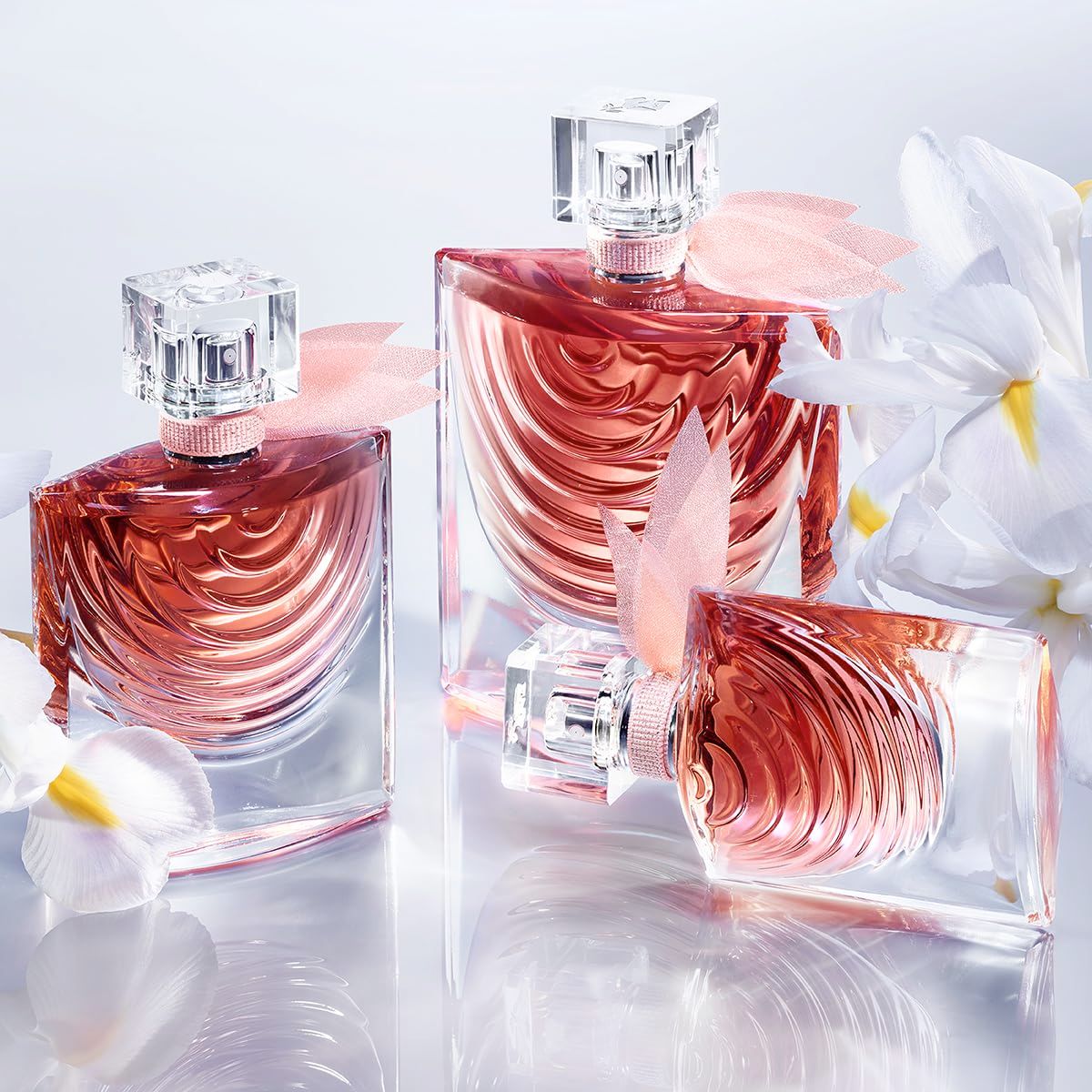 Tre flaconi con liquido rosa, vaporizzatore, nastro rosa e decorazione. Fiori bianchi.