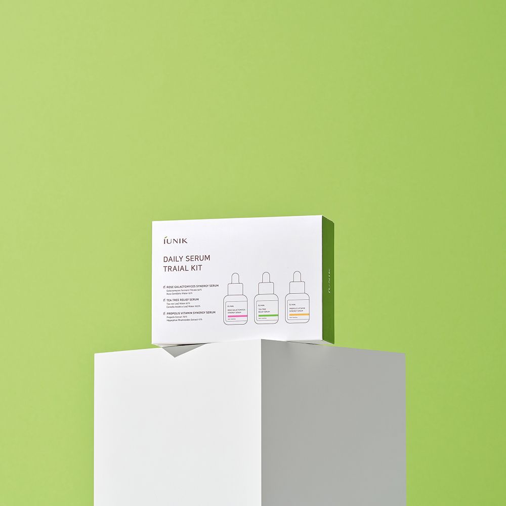 Confezione del prodotto su piedistallo bianco davanti a sfondo verde. Testo: iUNIK, Daily Serum Trial Kit. Tre illustrazioni di sieri.
