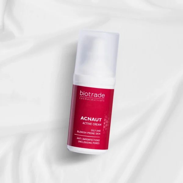 Flacone di crema con etichetta rossa su tessuto bianco. Testo: ACNAUT ACTIVE CREAM, per pelli grasse e impure. Anti-imperfezioni.