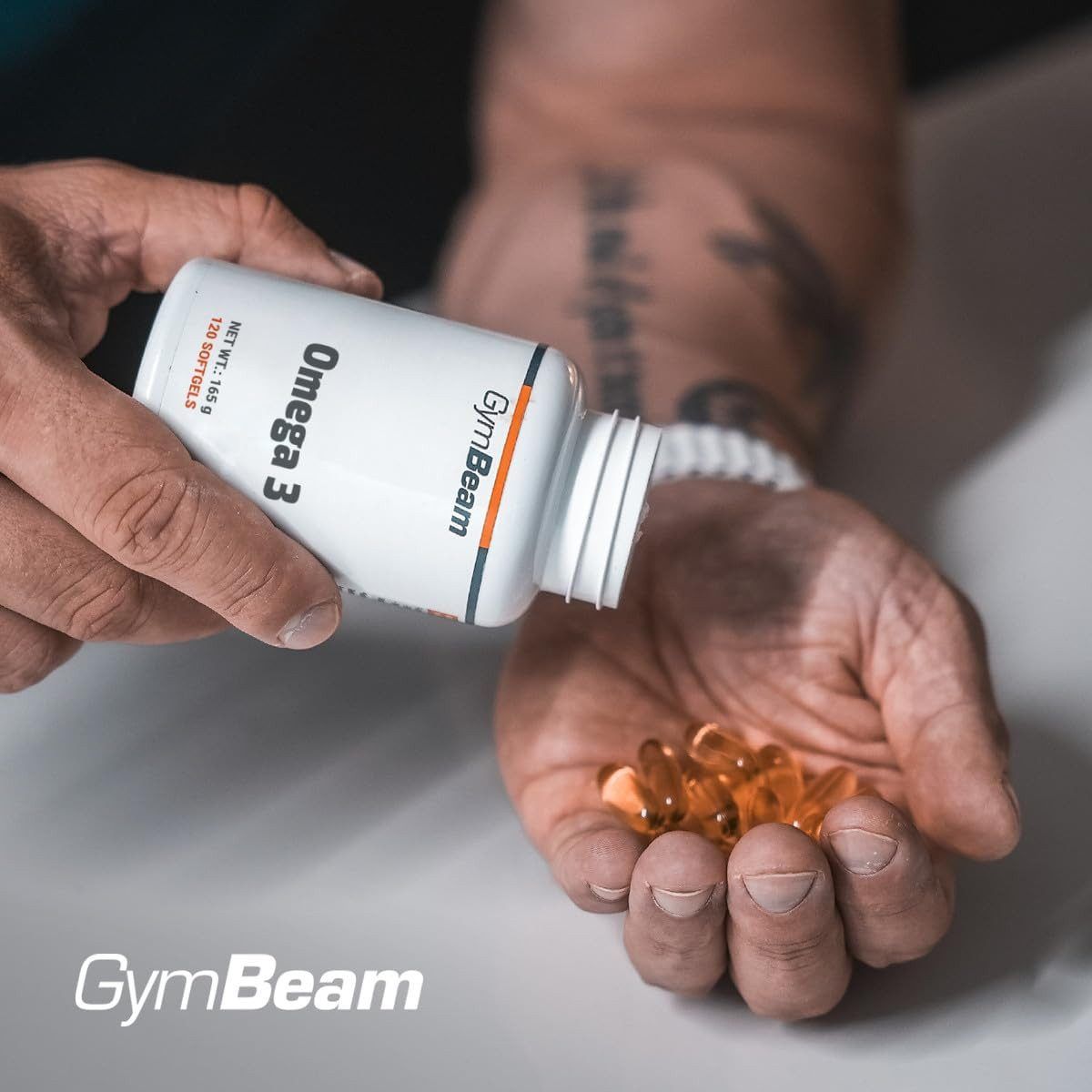 Una mano versa capsule GymBeam Omega 3 da un contenitore nell'altra mano.