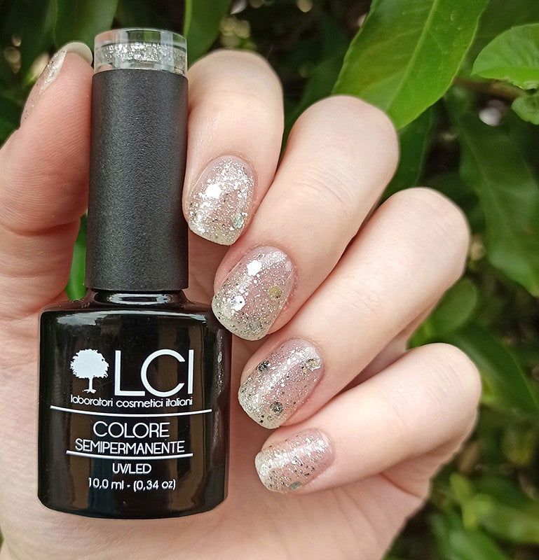 Flacone di smalto e unghie smaltate. Flacone nero con logo e testo. Unghie con smalto glitterato, tenute in mano.