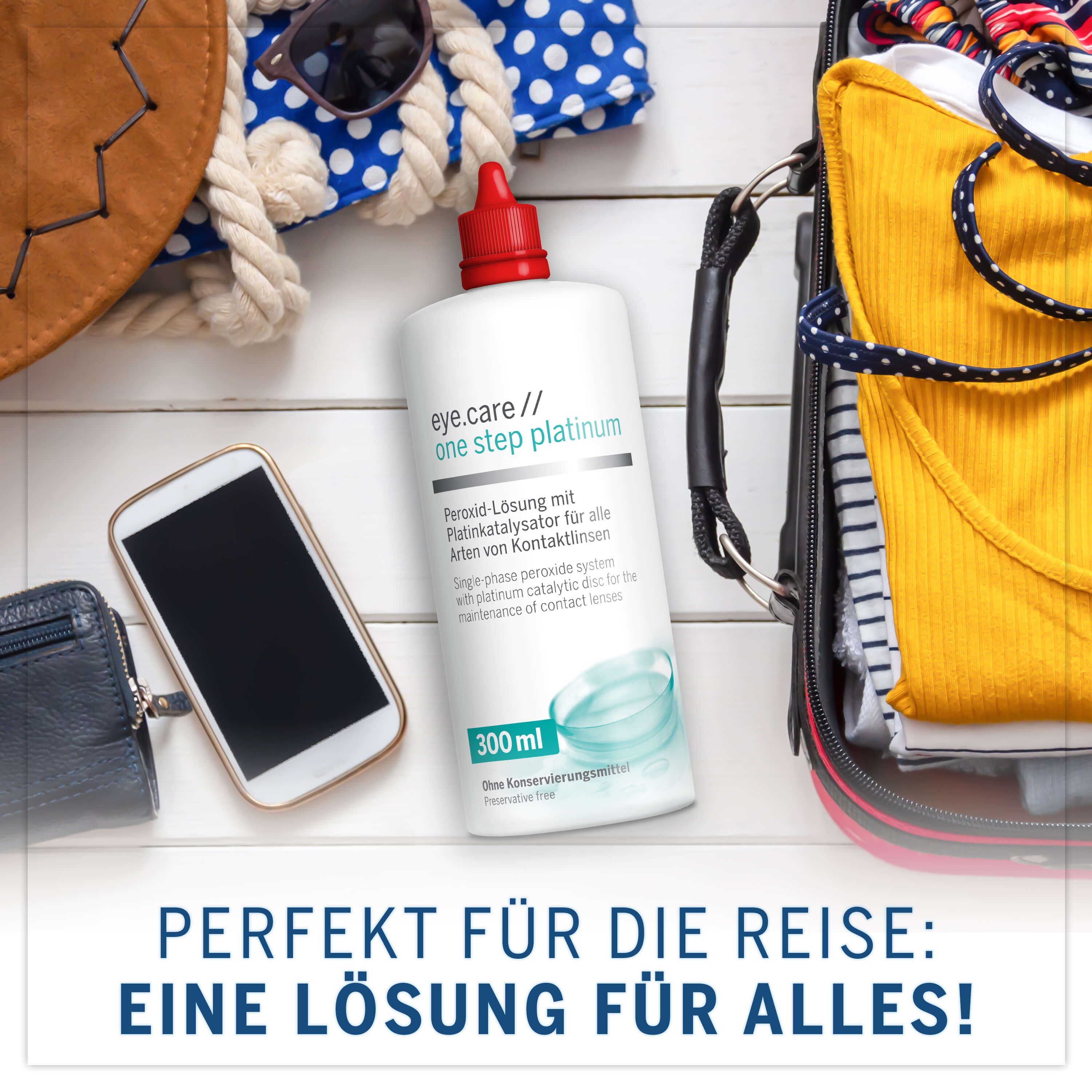 Flacone eye.care one step platinum, tappo rosso, 300 ml. Su valigia, accanto a telefono e portafoglio. Perfetto per viaggiare.
