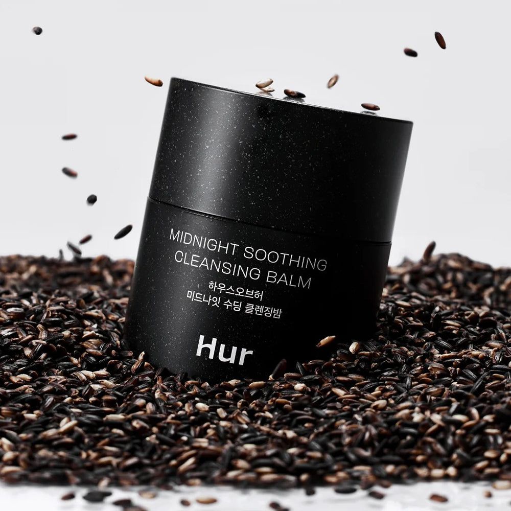 Barattolo nero con scritta: Midnight Soothing Cleansing Balm. Marchio: Hur. Circondato da semi neri. Sfondo bianco.
