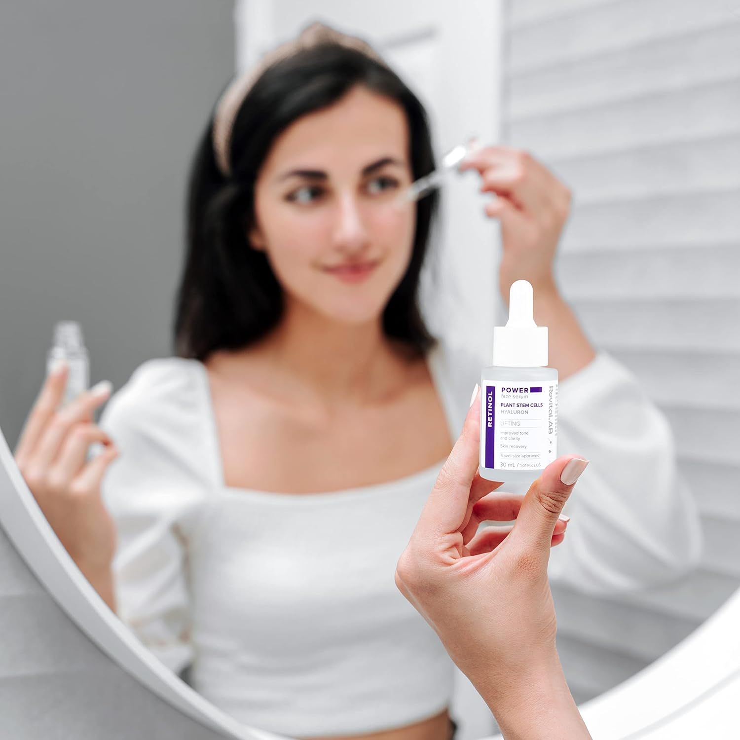 Donna tiene flacone di siero davanti allo specchio. Flacone con scritta: RevitaLAB, POWER face Serum, Retinolo, cellule staminali vegetali, Hyaluron.