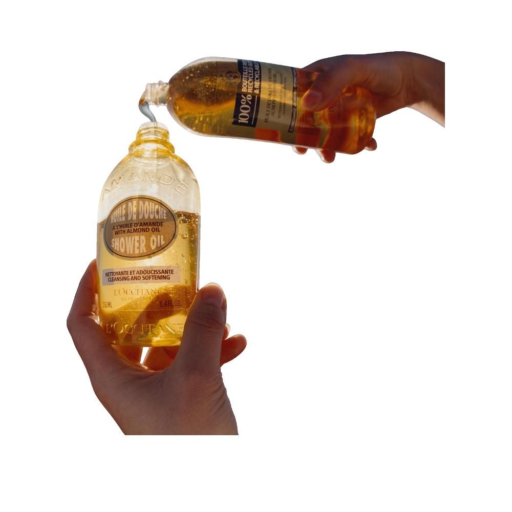 Mani che versano Olio Doccia Mandorla da una bottiglia in una più piccola. Etichetta visibile.