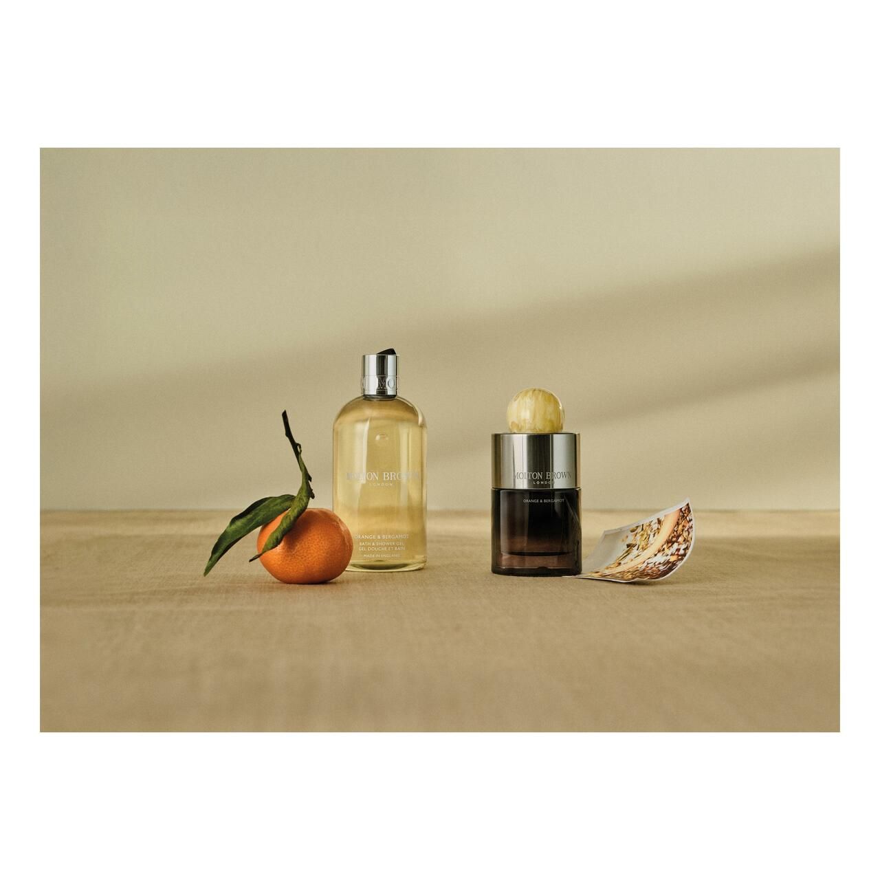 Natura morta con flacone, candela e mandarino. Su sfondo in legno chiaro. Prodotti Molton Brown.